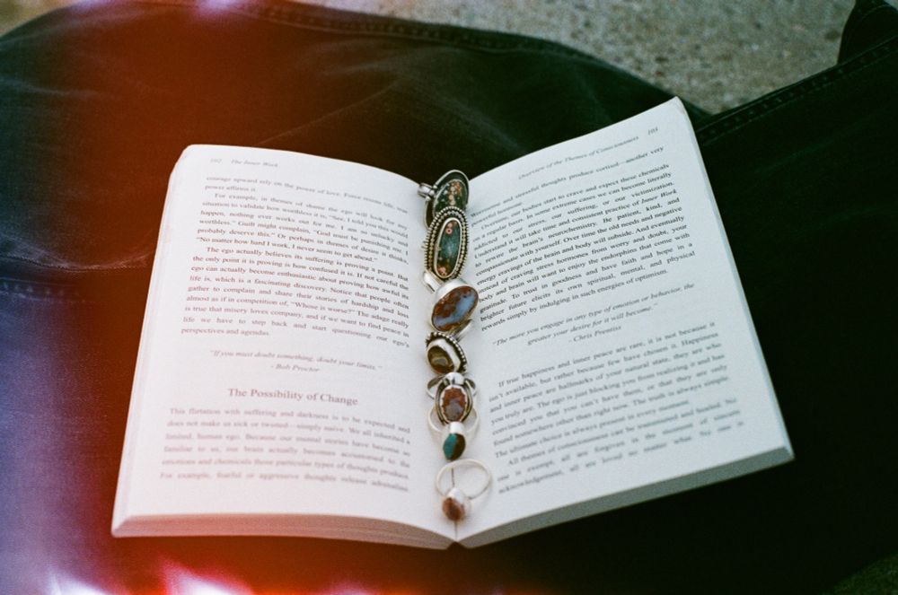 a film photograph of an open book with many rings sitting along the center. The rings are hand forged jewelry made of sterling silver and precious stones, made by Andisa Studio 