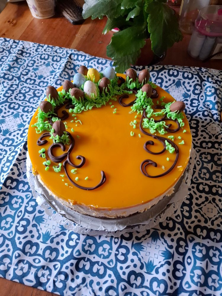A mango cheesecake decorated with chocolate swirls, green sugar cream grass and chocolate eggs. Made it myself!