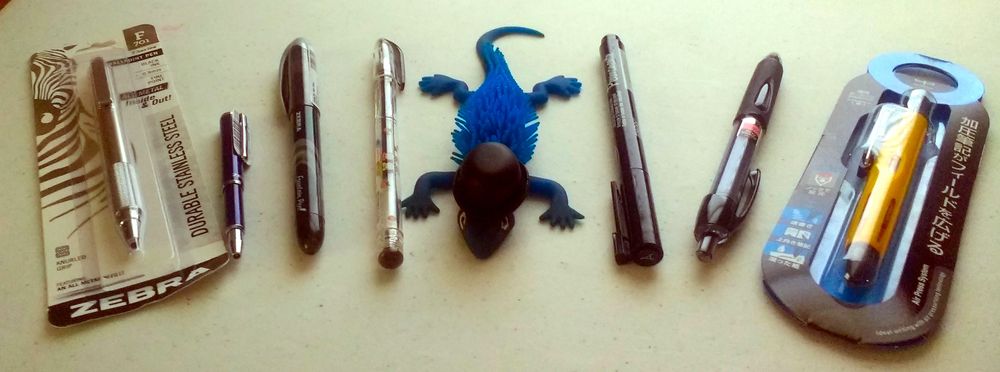 Blue Lizard is wearing a bowler hat. On both sides of him, there are an assortment of pens.