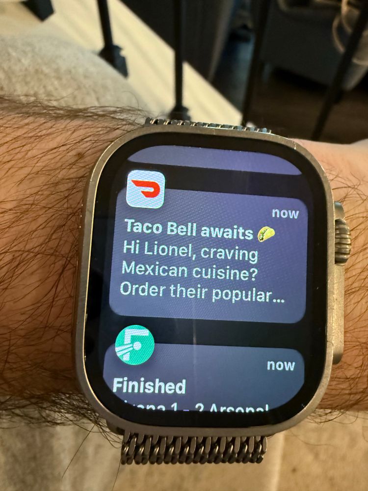 A photo of an Apple Watch showing a DoorDash notification inviting the user to buy Taco Bell even though the user has food at home. 