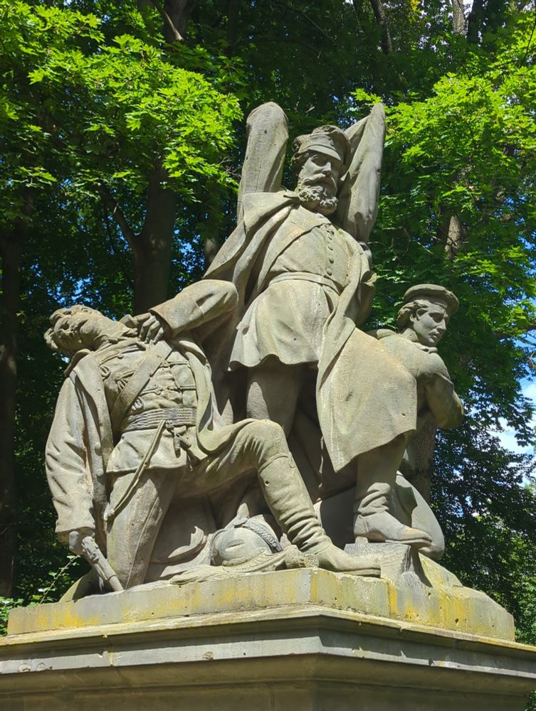 A statue of three men in a battle. The left has been shot, the middle is about to strike downwards, the right is drawing his sword. 