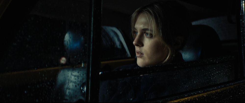 Nahaufnahme einer jungen Frau mit heller Haut und hellblondem Haar, die nachts auf dem Fahrersitz eines Autos sitzt.