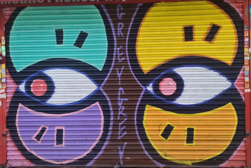 Graffiti picture of cartoon eyes on a shop front barriers. "GREY GREY" is written between the eys.