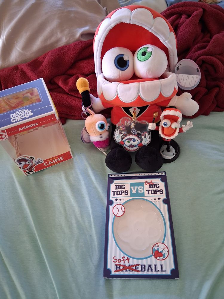 A zoomed out photo to show off all my TADC merch that I have, including the boxes of the Animatez and the Caine Shaker Keychain that has a baseball/softball theme to it. My Caine Plush has a Kinger Plush Keychain hanging on his cane, a Caine Shaker Keychain resting on his legs and a Caine Animatez on his right.
