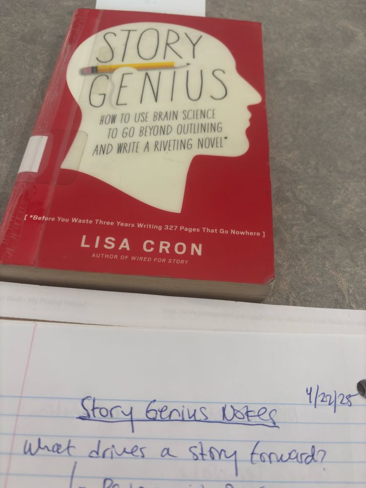 The book Story Genius by Lisa Cron is resting atop a gray library table. Beneath we see a glimpse of pages of a spiral bound notebook with handwritten notes in blue ink that reads “Story Genius Notes 4/22/2025 what drives a story forward?”