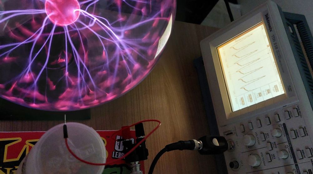 Setup to measure potential drop from a plasma ball.  Showing glowing ball and antenna and oscilloscope.