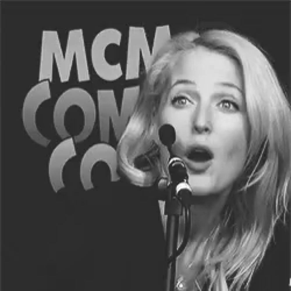 a woman singing into a microphone in front of a mcm con logo