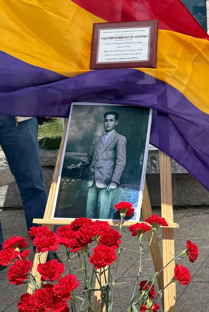 Atril de madera con una fotografía de Valentín Barroso de Antonio en traje con una placa dedicada a él sobre la bandera republicana. Delante, claveles rojos a forma de ofrenda floral. 
