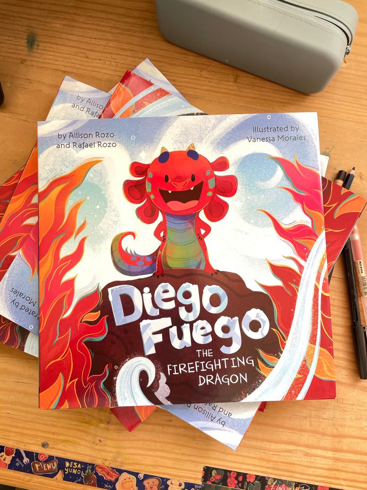 Picture of the cover of DIEGO FUEGO, The Firefighting Dragon : a little axolotl-like red dragon standing in the middle of the cover with some snow flurries and flames around him, fun! 