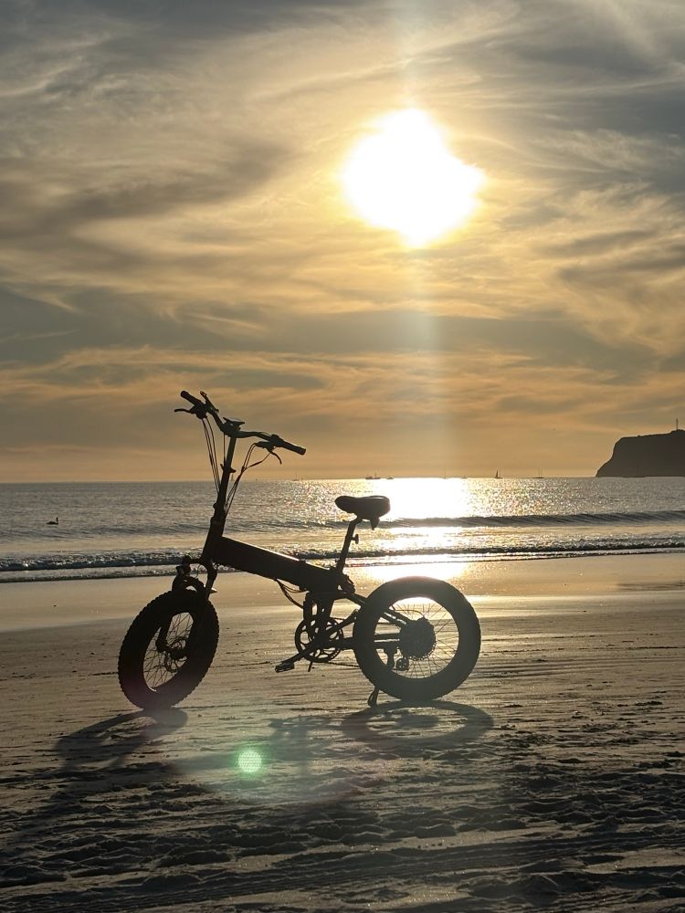 A random e bike parked on the beach with the sun and ocean and Point Loma behind it