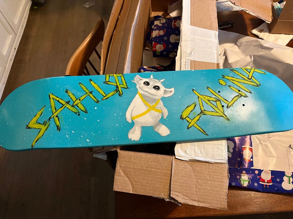 A skateboard deck painted SAI blue, with NED being his adorable self, wearing yellow bandito tape, and the words SAHLØ FØLINA in yellow. ITS SO FREAKING COOL

It’s balanced on the box Jac shipped it in, on my kitchen table, surrounded by Christmas wrapping paper 