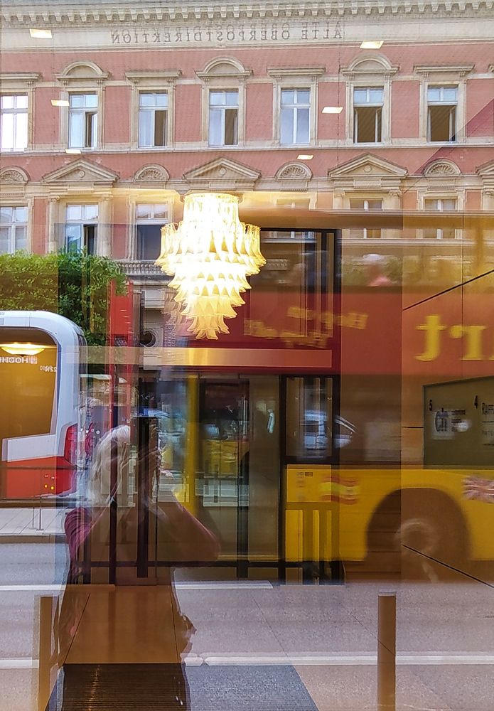 Straßenszene, durch Spiegelung in einem Fenster fotografiert. Lück zwischen einem roten Bus und einem gelb-roten Doppeldecker 
