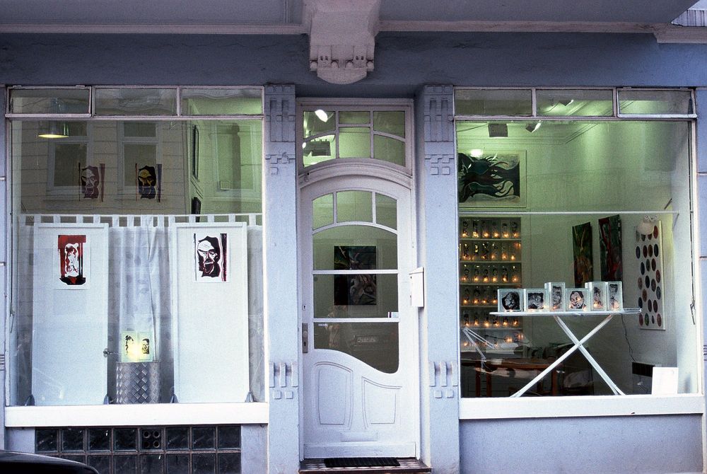 Schaufenster und mittige Tür eines Ladens mit Altbau-Charakter. In und durch die beiden Schaufenster sind Kunstwerke zu erkennen.