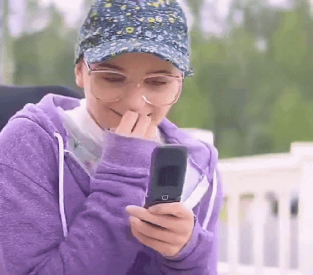 a woman wearing glasses and a hat is holding a flip phone .