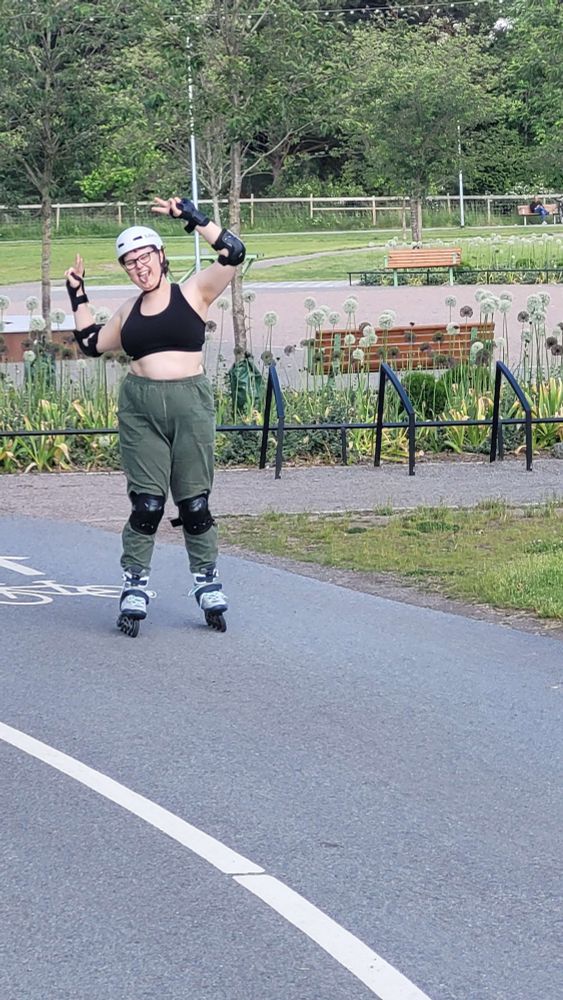 butch rollerskating in a park, doing peace signs and sticking tongue out
