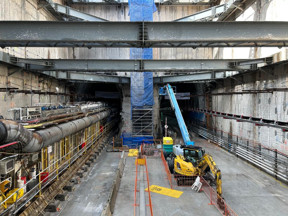 Looking towards the eastern wall of the under-construction station box for the Parramatta metro station from part of the way down, with 2 tunnels continuing past the wall and the back section of a tunnel boring machine on the left side