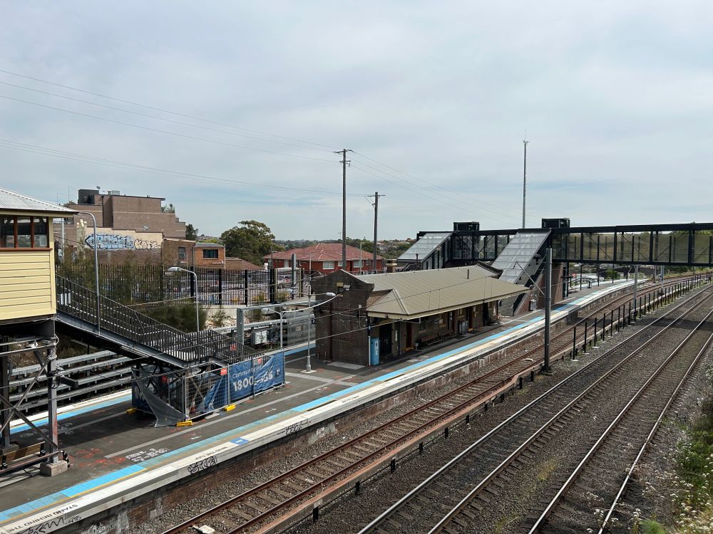 A view of Dulwich Hill Station from the Wardell Road bridge in late September 2024. The station has an island platform and a brick building in the center.
