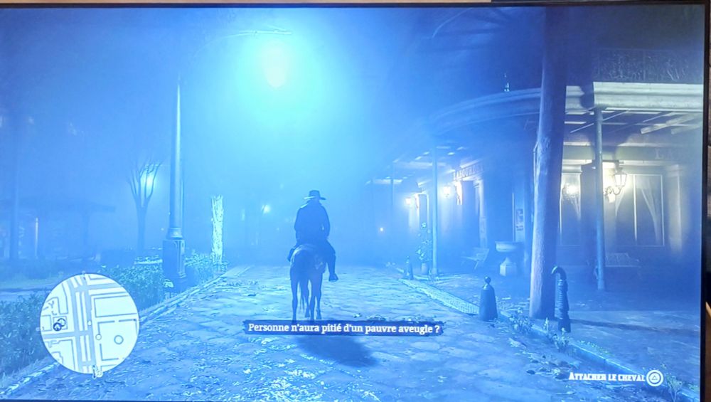 Screenshot du jeu vidéo Read Dead Redemption 2 de Rockstar. Là le héros est sur son cheval la nuit dans la ville de Saint-Denis, une évocation de La Nouvelle Orléans fin XIXè début XXè. Il y a une lumière électrique très brillante en haut de l'image.