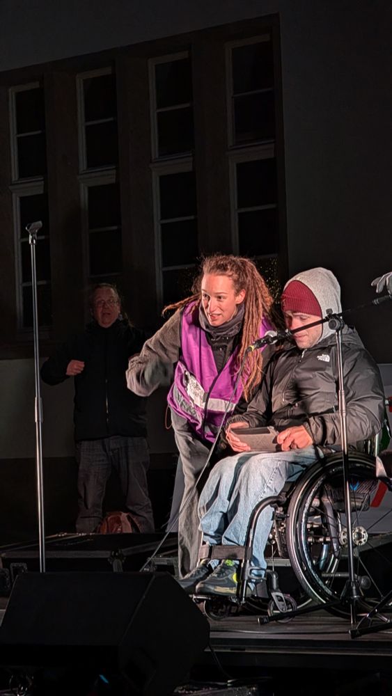 Rollstuhlfahrer in Winter Kleidung mit Kapuze auf einer Demo Bühne