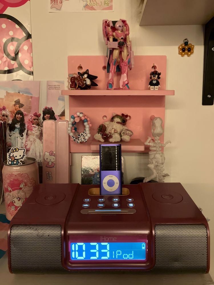 focus on a purple ipod docked in a pink ihome iH5. various pink trinkets surround