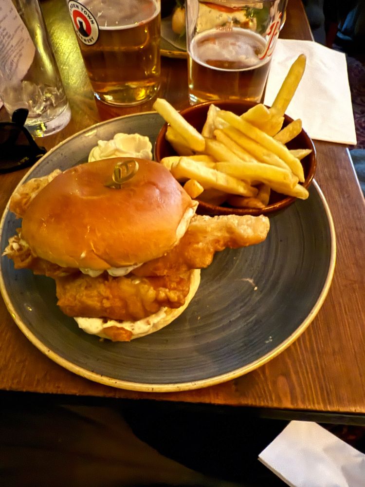 a fish finger sandwich with a small bowl of chips