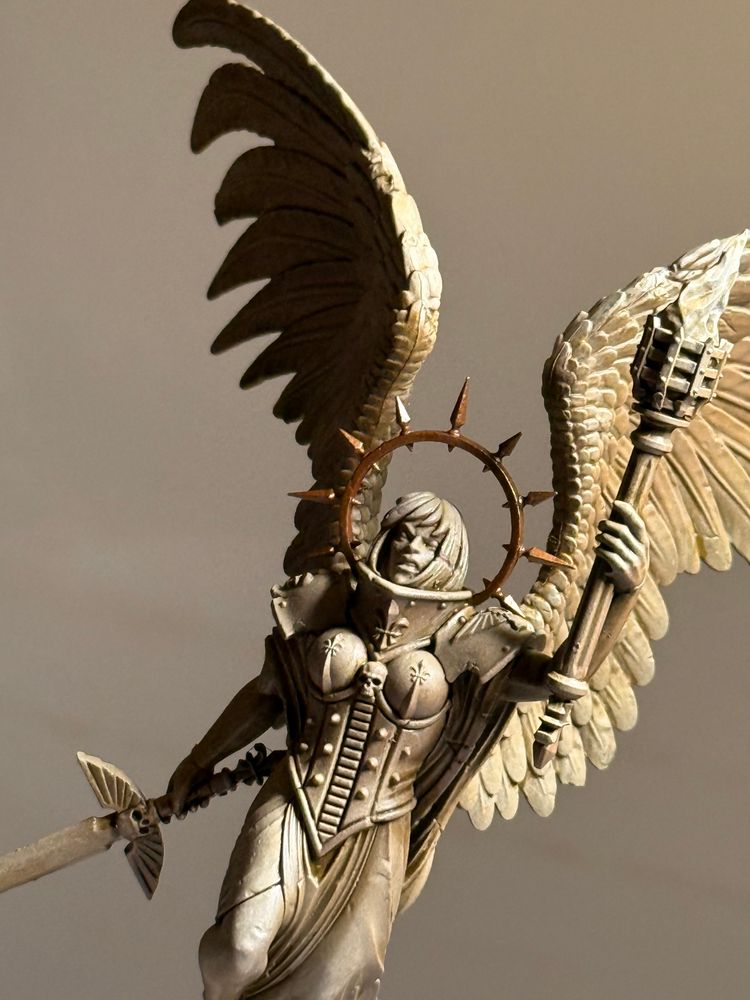 A detail of a 28mm-scale statue of a winged figure holding a torch and sword, with a spike brass halo 