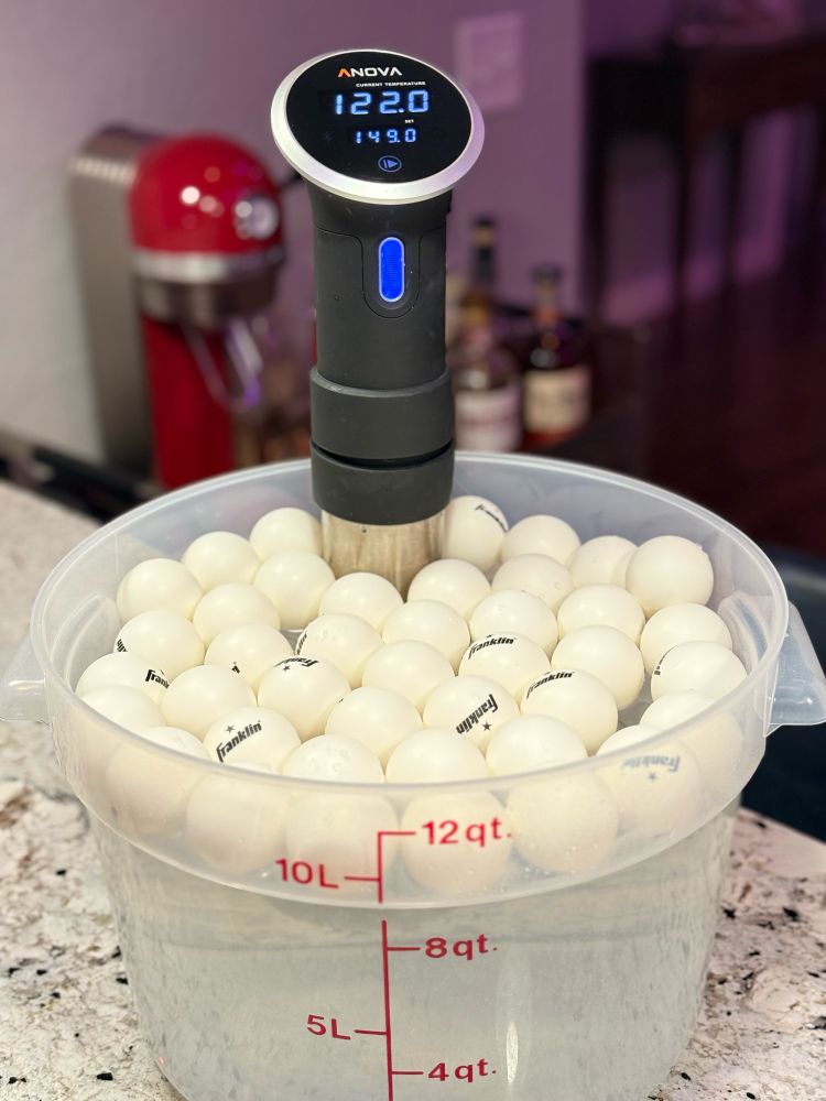 Ping pong balls float on the surface of a 12 qt. Cambro container, trapping heat and steam and returning it to the sous vide bath.