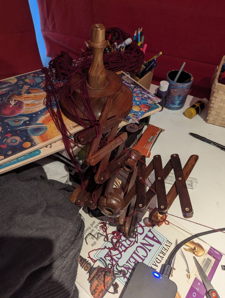 Burgundy yarn is tangled in the remains of a tabletop swift, which has come apart into individual pieces.