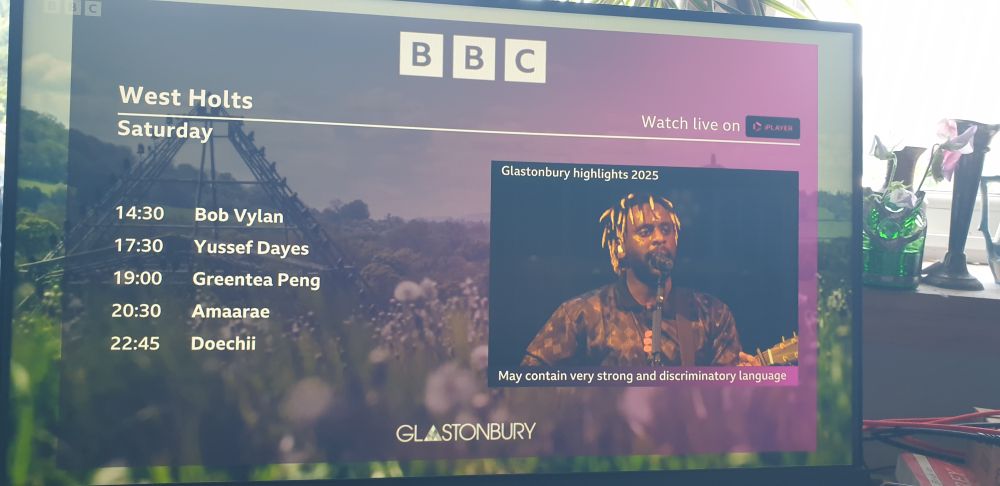 A photo of the BBC iPlayer between-sets holding screen for the #WestHolts stage at #Glastonbury2025. It reads:
14:30 Bob Vylan
17:30 Yussef Dayes
19:00 Greentea Peng
20:30 Amarae
22:45 Doechii

They have explicitly omitted:
16:00 #Kneecap