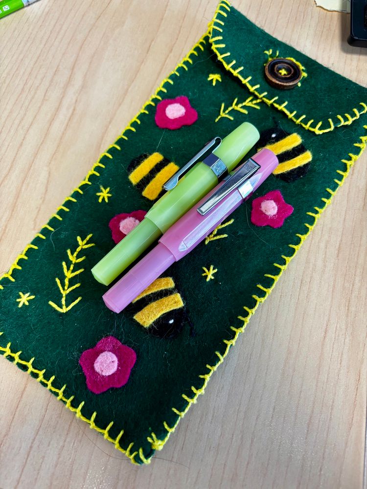 Two Kaweco sport fountain pens. One is pink, the other is green. They are resting on a felt pencil case.