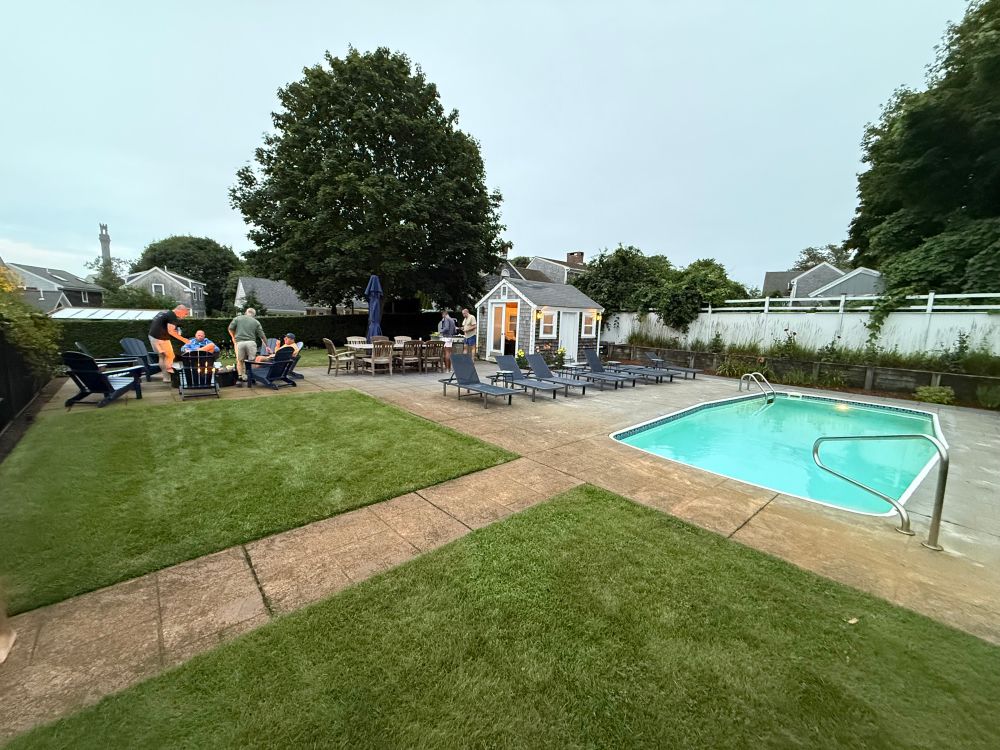 A photo of the backyard at my Provincetown rental house, showing a pool, a pool house, a fire pit, a large table and a grill