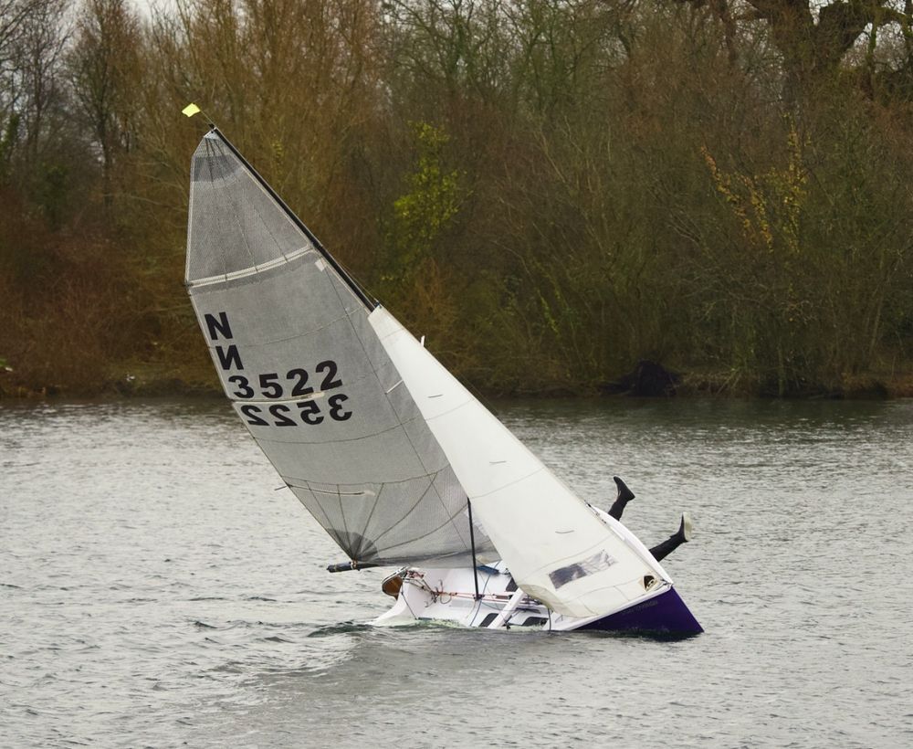 A National 12 capsizing to starboard whilst a pair of legs disappear in comic fashion to port.
