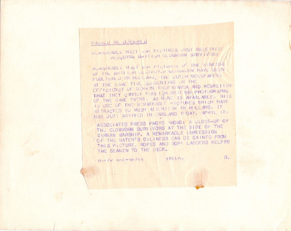 Rear of photo of Glowworm survivors. Associated Press stamp, with following press release stuck over it: 
"Passed as censored. Remarkable Nazi war pictures just received: rescuing British Glowworm survivors.
Remarkable Nazi war pictures of the sinking of the British destroyer Glowworm have been published in Holland, the Dutch newspapers at the same time commenting on the efficiency of German propaganda and regretting that they cannot publish British photographs of the same event, as none is available. This is one of the remarkable pictures which have attracted so much attention in Holland. It has just arrived in England today, April 18.
Associated Press photo shows: a close-up of the Glowworm survivors at the side of the German warship. A remarkable impression of the water's oiliness can be gained from this picture. Ropes and rope ladders helped the seaman to the deck."