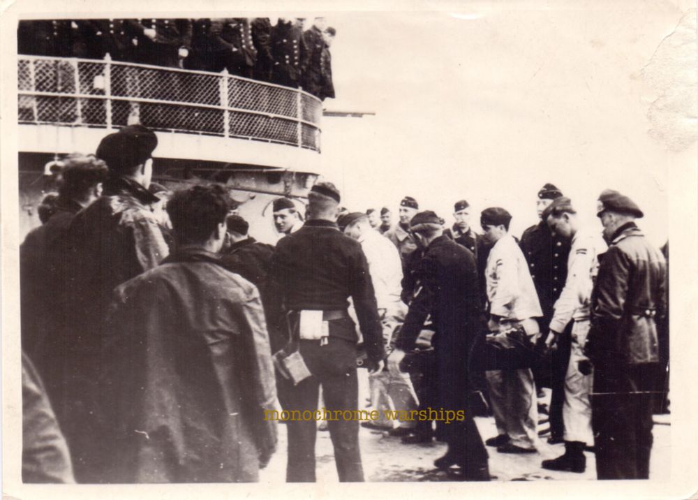 Crew of one of the Scharnhorsts gather to watch a wounded sailor brought aboard on a stretcher. An interesting selection of uniforms suggesting crew members from various different departments of the ship are taking an interest in proceedings.
