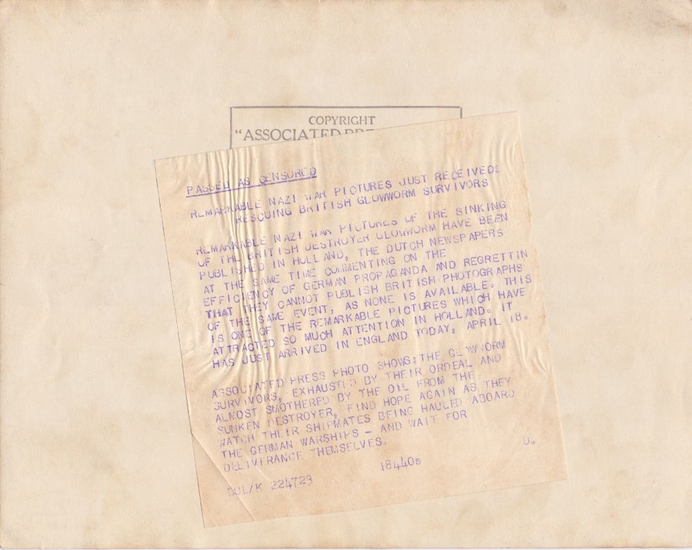 Rear of photo of Glowworm survivors. Associated Press stamp, with following press release stuck over it: 
"Passed as censored. Remarkable Nazi war pictures just received: rescuing British Glowworm survivors.
Remarkable Nazi war pictures of the sinking of the British destroyer Glowworm have been published in Holland, the Dutch newspapers at the same time commenting on the efficiency of German propaganda and regretting that they cannot publish British photographs of the same event, as none is available. This is one of the remarkable pictures which have attracted so much attention in Holland. It has just arrived in England today, April 18.
Associated Press photo shows: the Glowworm survivors, exhausted by their ordeal and almost smothered by the oil from the sunken destroyer, find hope again as they watch their shipmates being hauled aboard the German warships - and wait for deliverance themselves."