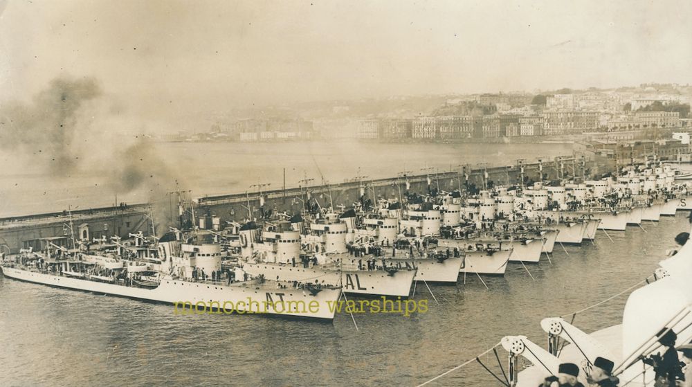 A lot of Spica class torpedo boats of the Regia Marina lined up, sterns to the quayside, at Naples, post October 1938. There's a lot of Spicas. I mean, there's Spicas as far as the eye can see. I count fourteen but there may be more. They are being reviewed by some blackshirt types on a vessel that is passing by. Boo them. Boo the blackshirts. Boo!!!!