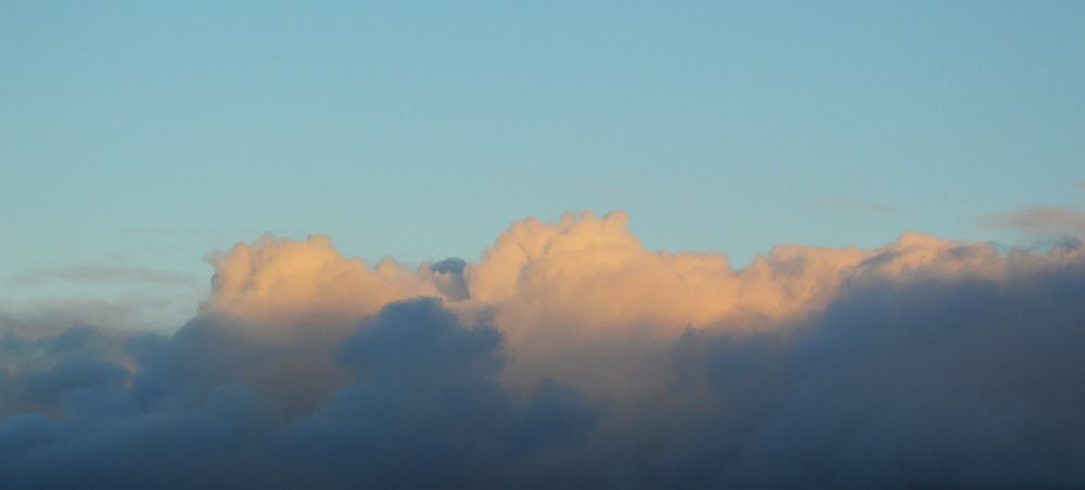 Strong warm yellow and orange evening sunlight skims the tops of some dark blue crouds.
