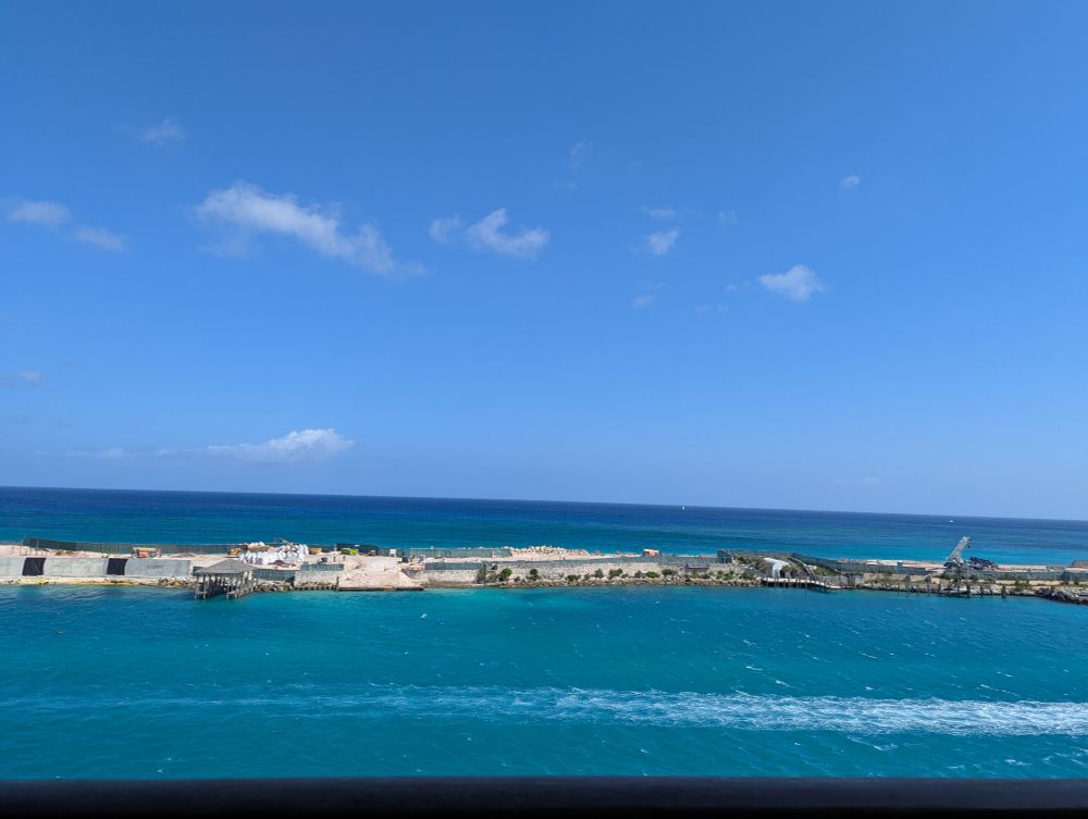 View of blue green water in the Bahamas and a strip of land with construction crews on it. 