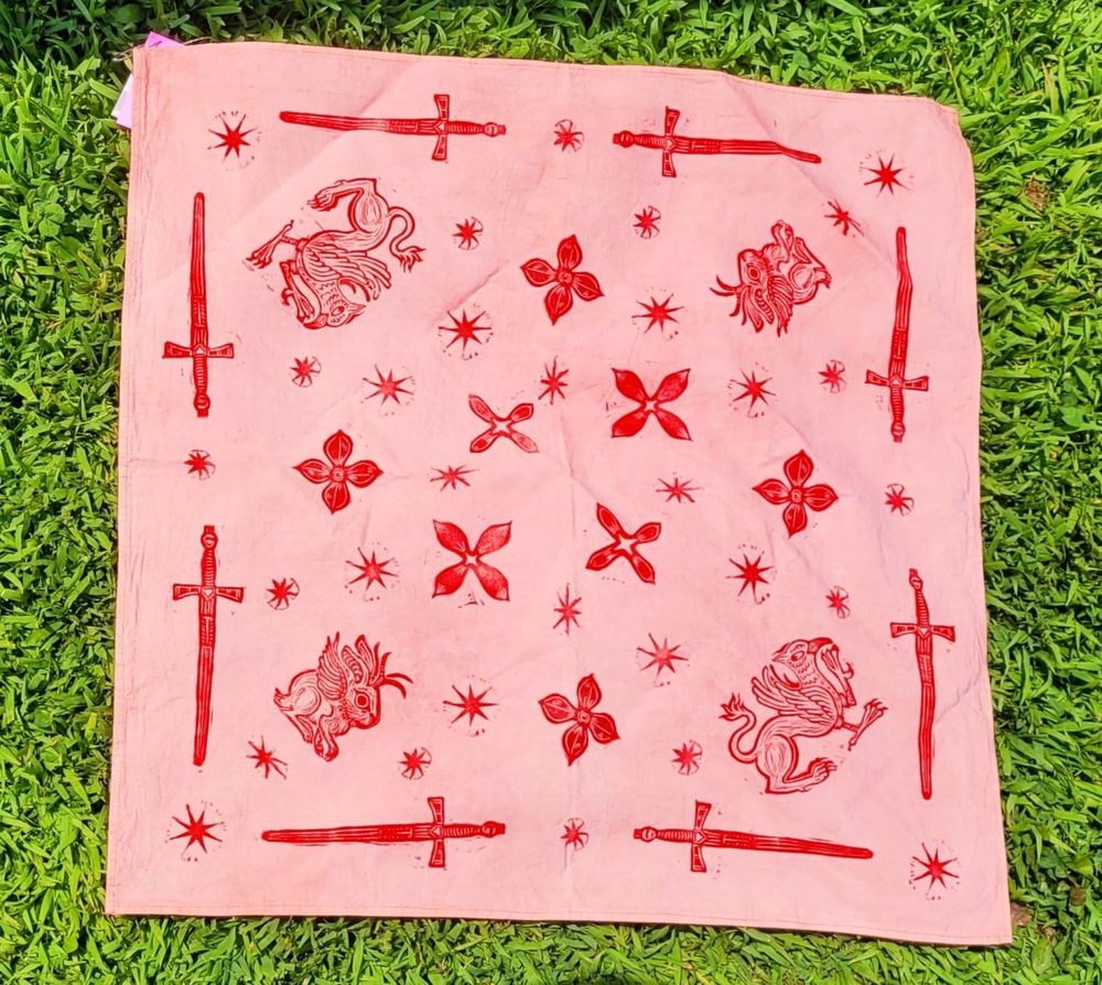 light pink-orange cotton bandana with red block prints of swords, flowers, stars, gryphons, and jackalopes