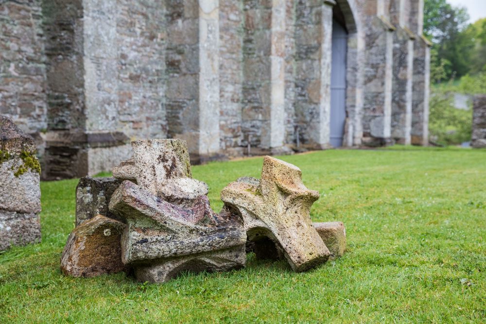 Ornate remains of traceried stonework from the medieval abbey beside the Great Barn on a lawn of bright green grass.