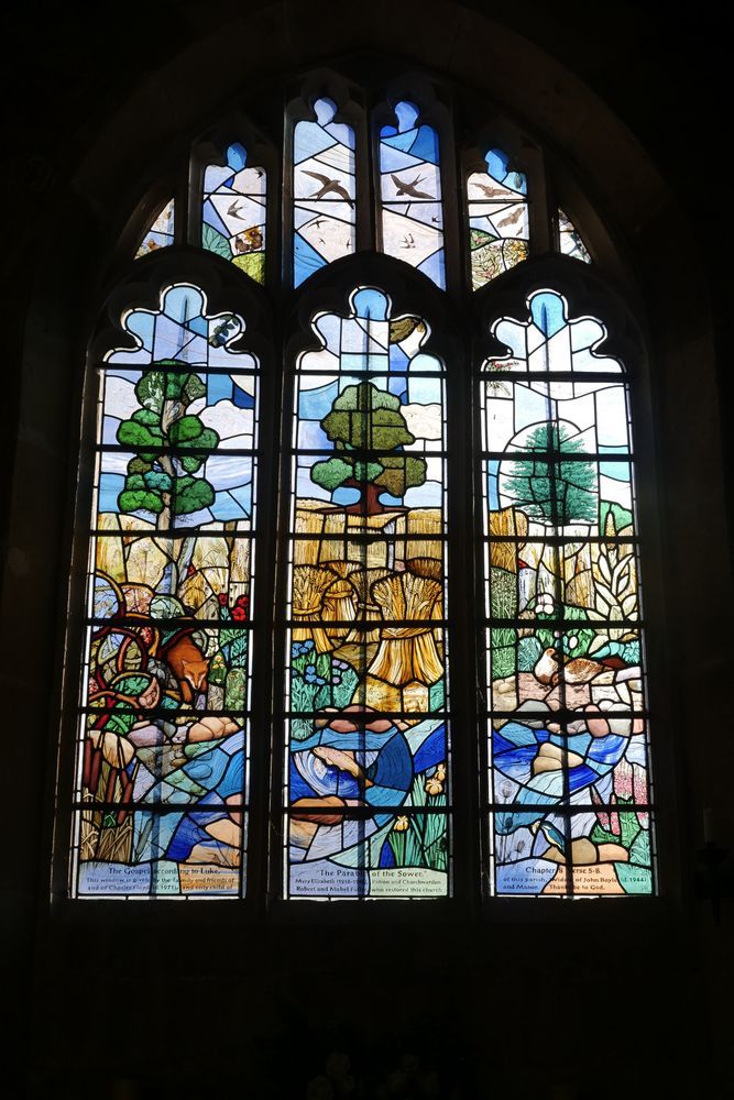 A stained glass window at a church at Great Chalfield Manner. The stained glass shows a country landscape with a river in the foreground and fields with trees in the background.