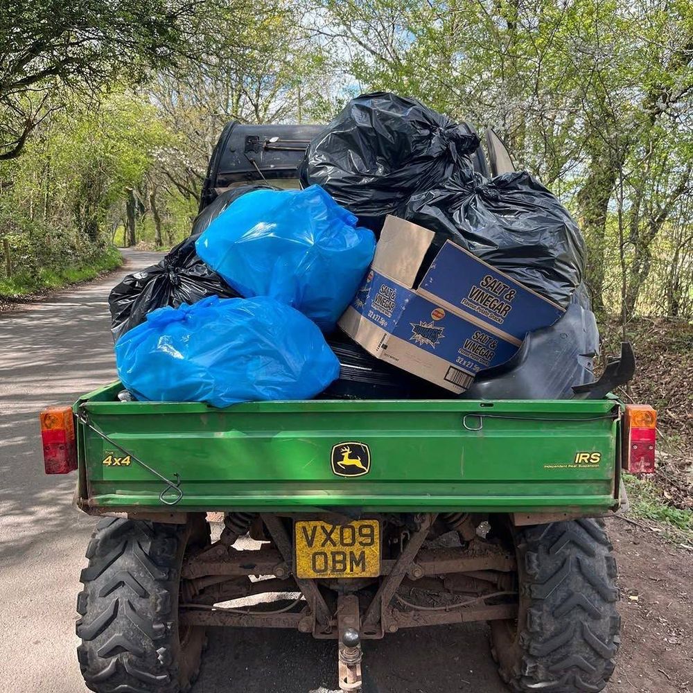 A green truck on a tree-lined street with mounds of collected rubbish piled on it