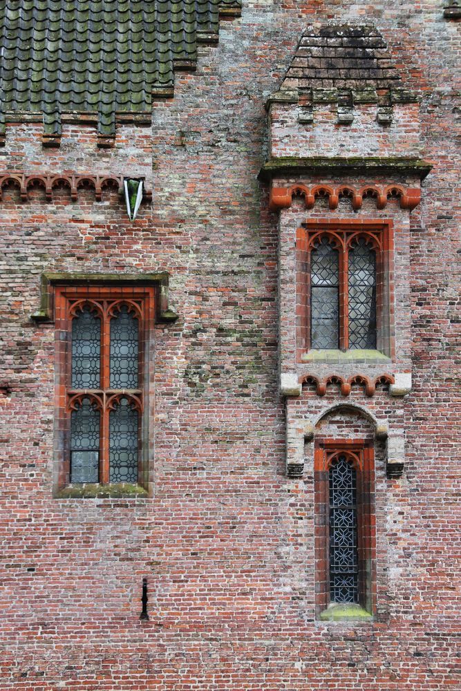 An image of brickwork and windows at Oxburgh Hall, Oxford. Three windows of different shapes are set into a red-brick wall.