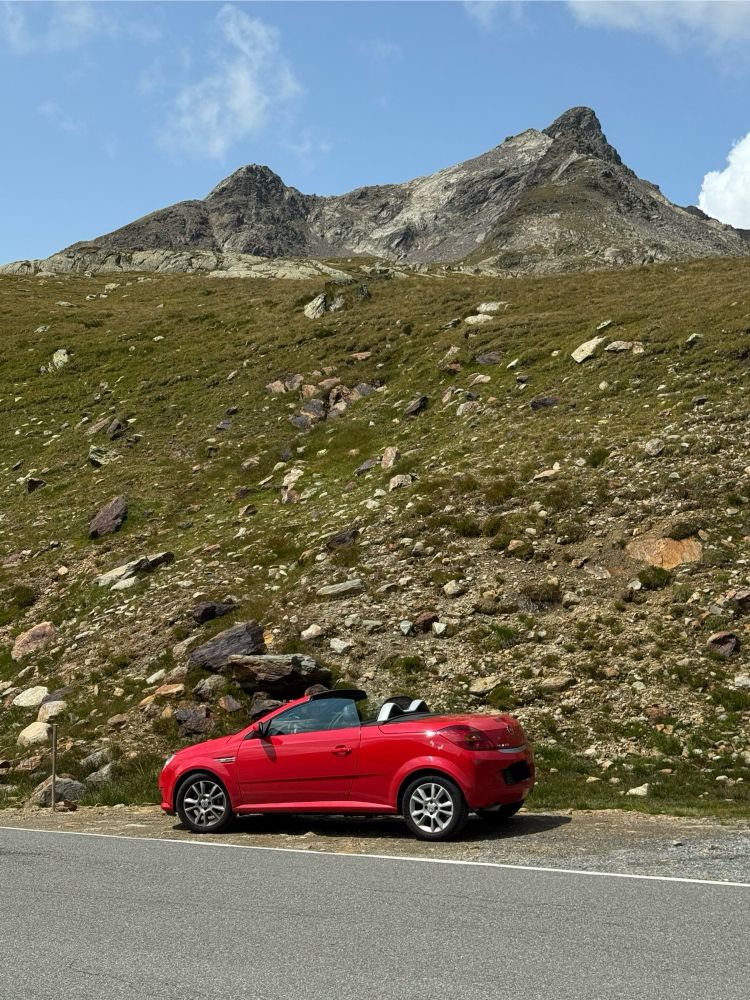 roter Opel Tigra mit offenem Dach vor Bergkulisse