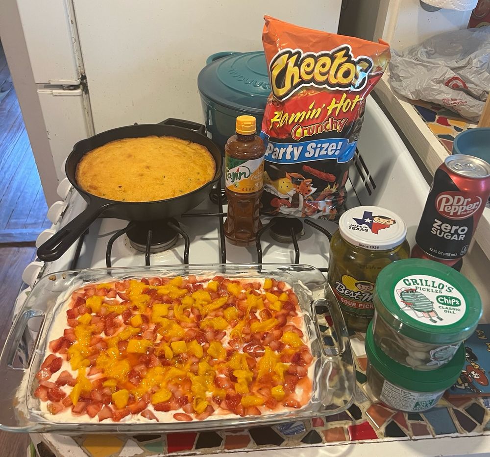 Food on display on an oven: jalapeño cheddar cornbread, mostachón cake, pickles, hot Cheetos, Tajín, Dr Pepper 