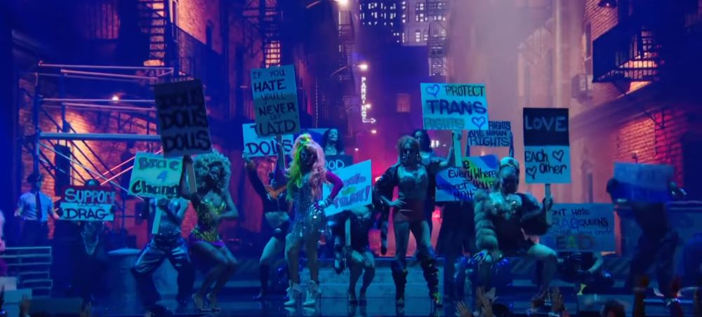 screencap from sabrina carpenter's vmas performance for tears in which a number of backup dancers are holding protest signs including "protect trans rights", "dolls dolls dolls", "support local drag", "if you hate you'll never get laid", "gay rights are human rights", "tip the dolls", and "for the shes the gays and the theys"