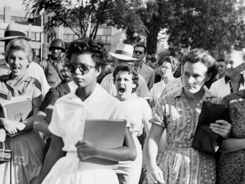 White onlookers denigrating a black student entering school during the civil rights movement.