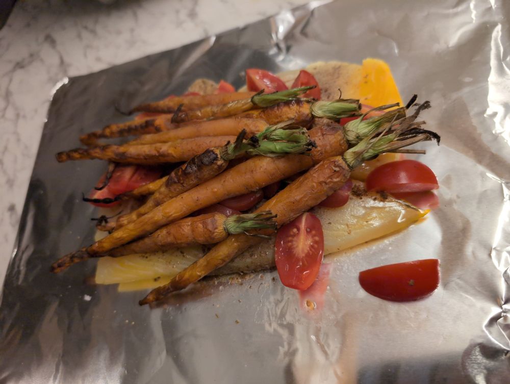 Smoked haddock sitting on foil with sliced cherry tomatoes, Indian spices and long fine carrots, ready to be wrapped in a foil bag and cooked with cream