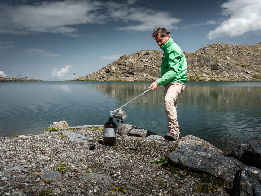 Der Schmiedingersee am Kitzsteinhorn. Davor ein Mann in grüner Greenpeace-Jacke, der Wasserproben in eine dunkle Glasflasche füllt.