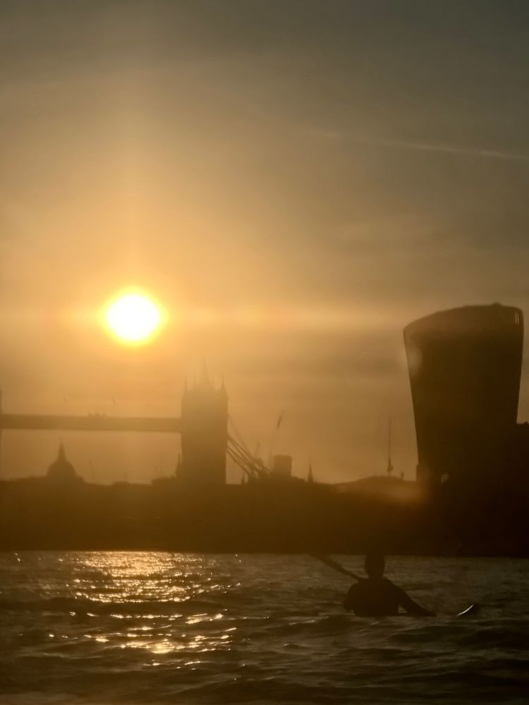The setting sun backlights tower bridge and a kayaker 